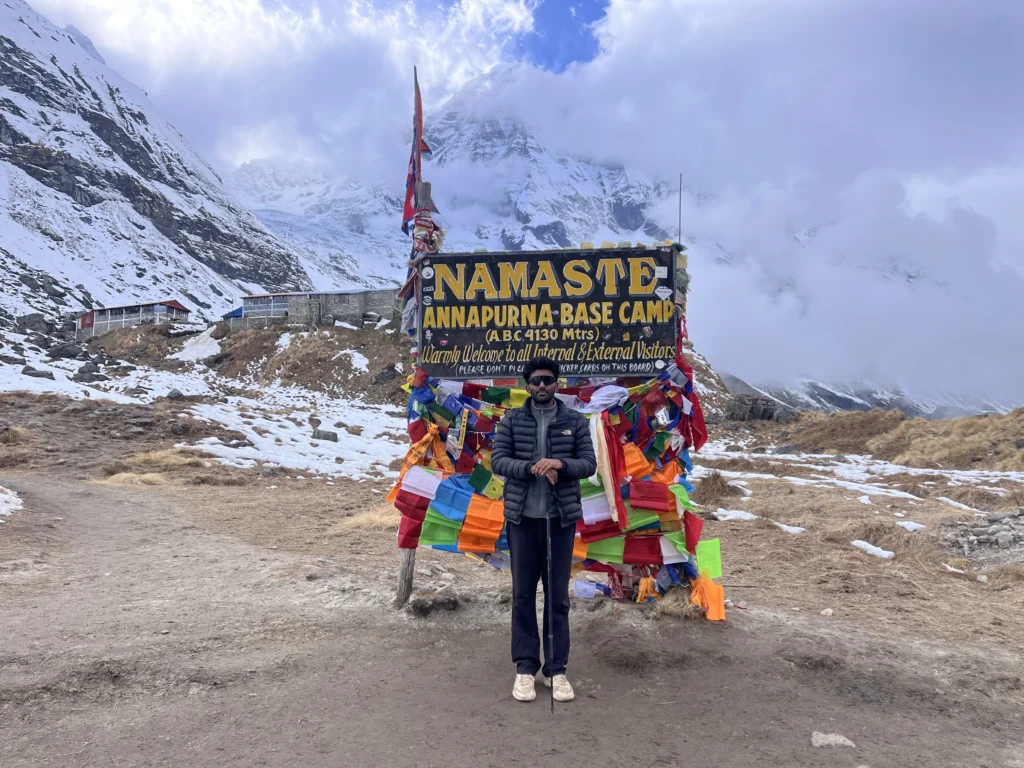 Trekker standing at the Annapurna Base Camp (ABC 4130m) signboard surrounded by snow-covered mountains during the Annapurna Base Camp trek